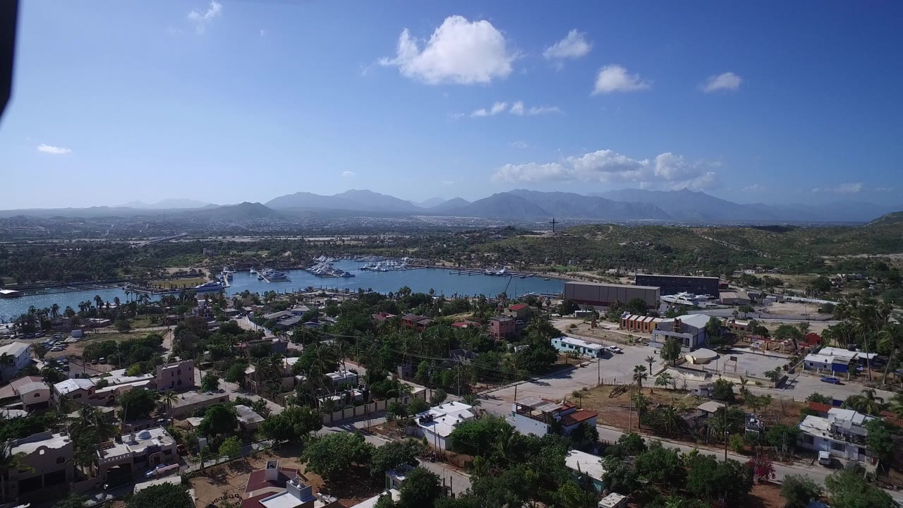 Aerial view over town, bay, hills, and distant mountains under blue sky