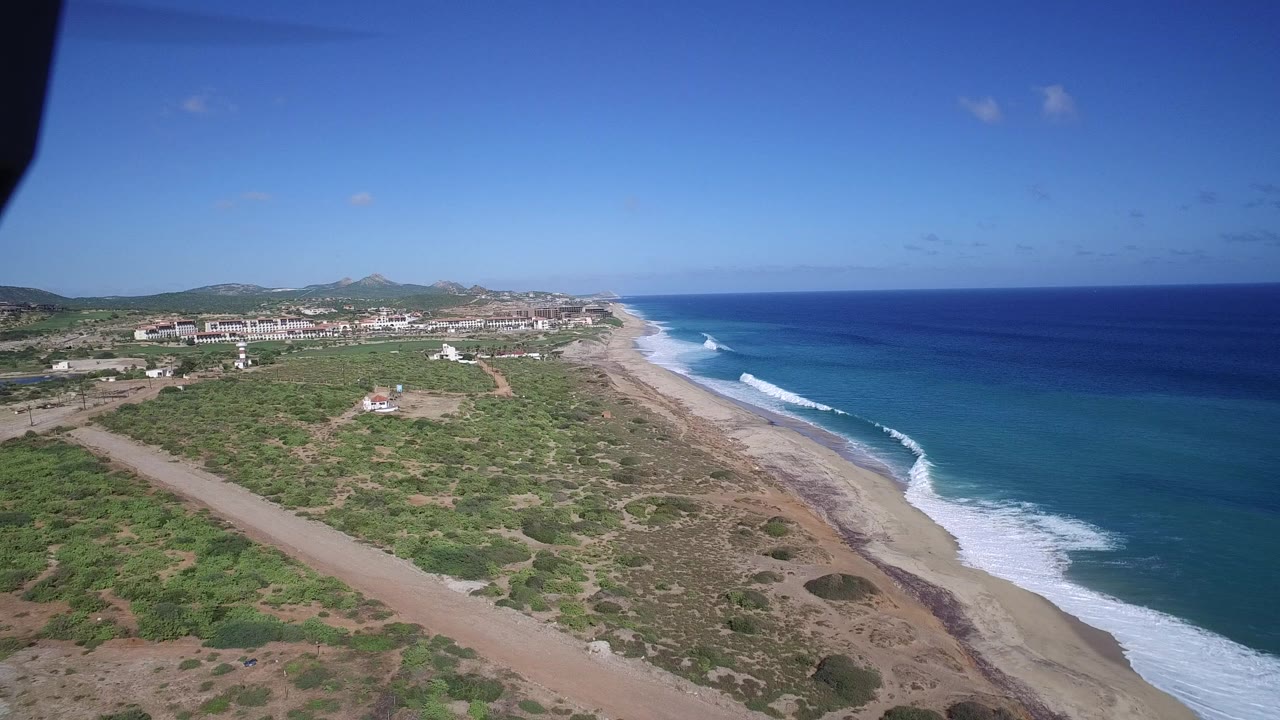 Aerial view of sandy coast, scrubland, and blue ocean surf.