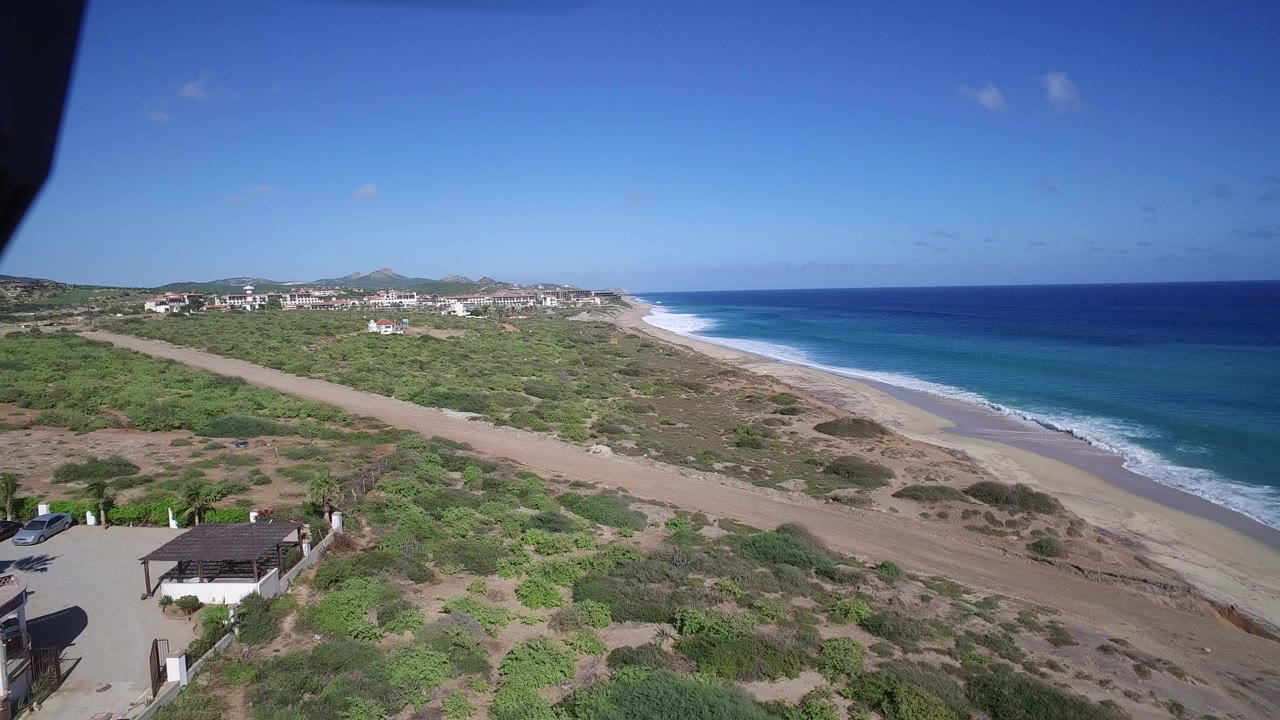 Elevated view of beach, ocean, scrubland, road, and coastal buildings.