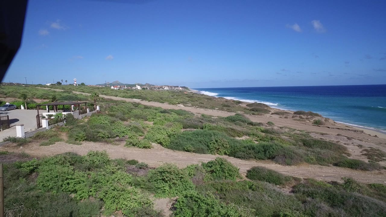 Ocean horizon beyond scrub-covered coastal terrain and nearby structures.