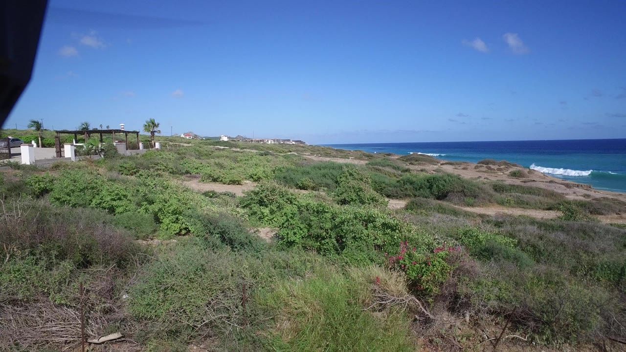 Playita hillside vegetation fills the foreground while houses sit on the left ridge and the ocean runs across the background, with no visible people.