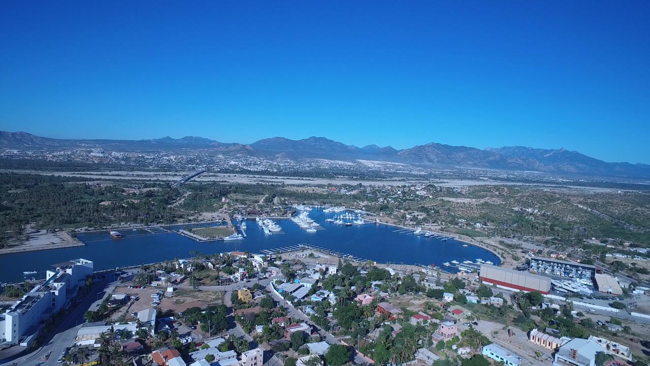 High aerial view of marina water, coastal houses, roads, and distant mountains.