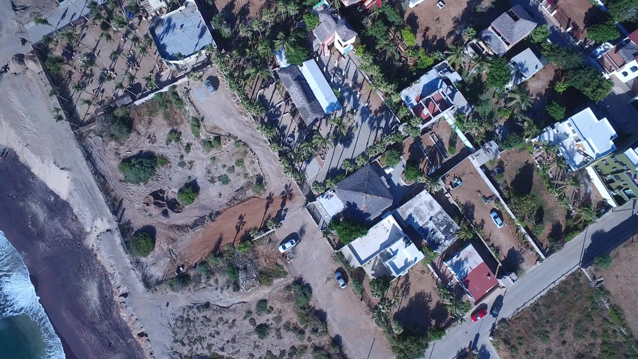 Overhead coastal neighborhood beside a narrow beach and surf.