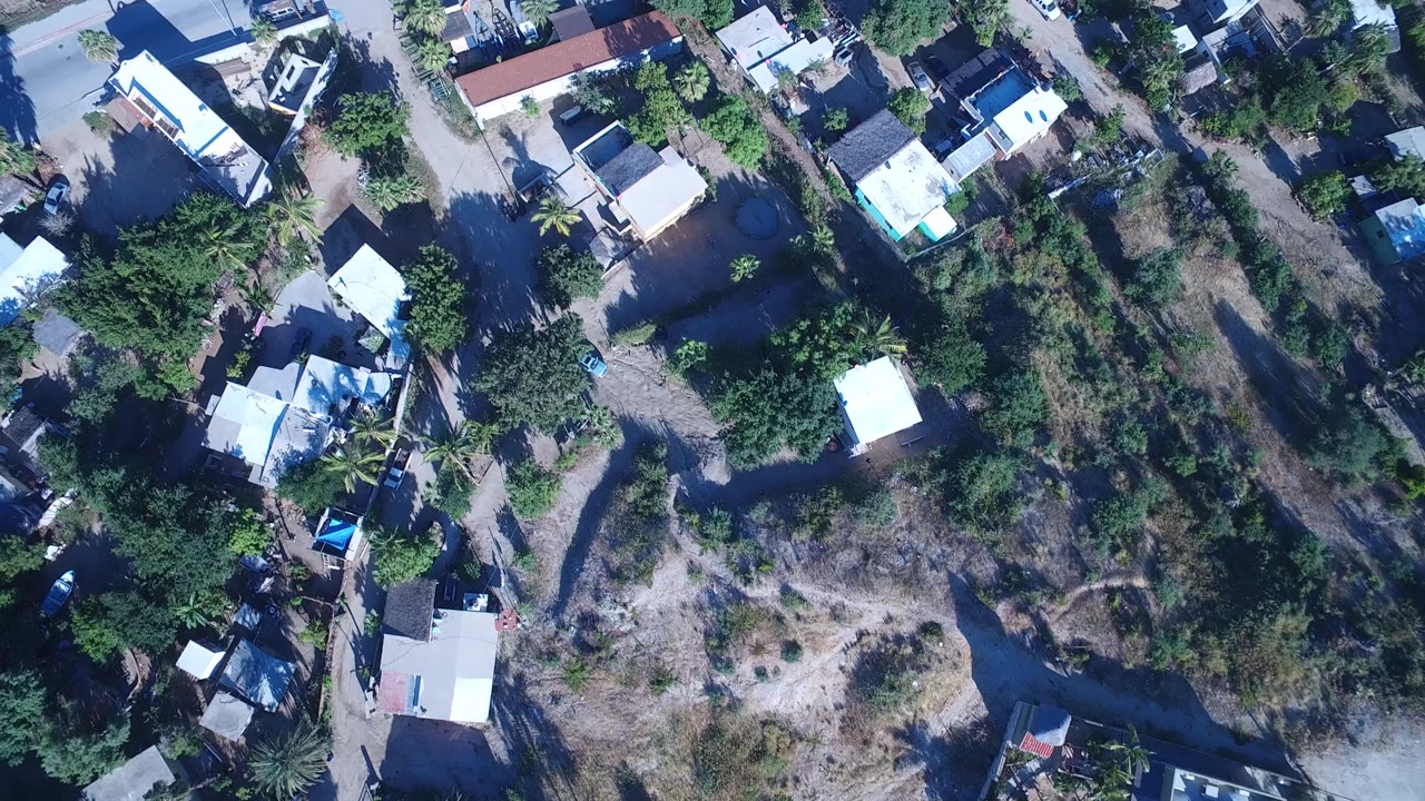 The second frame holds above Playita with more of the road grid, white rooftops, trees, open dirt lots, and a small section of green water visible, with no visible people.
