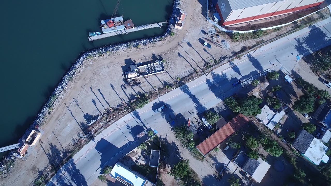 Overhead view of green water, shoreline road, docks, boats, and low buildings.
