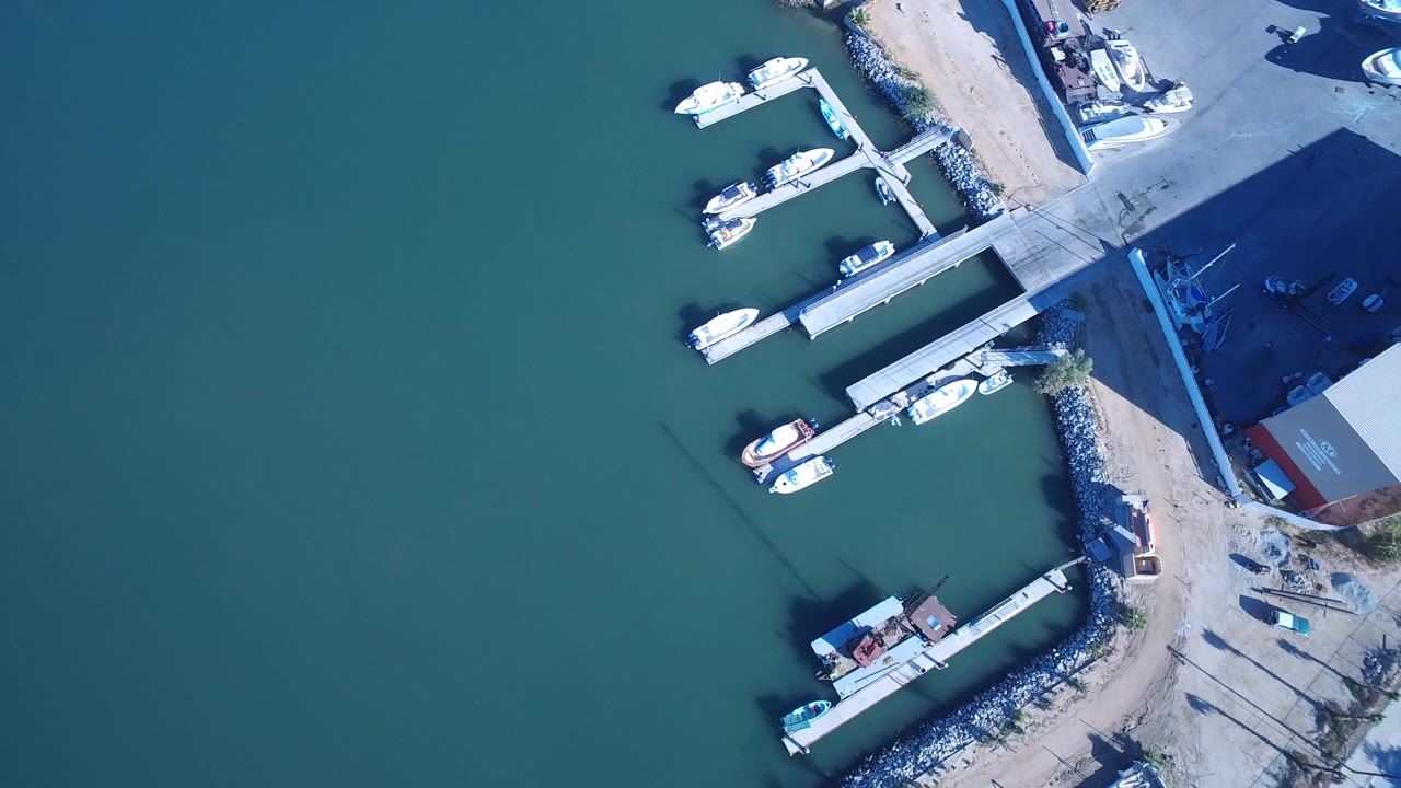 Aerial view over Playita harbor with blue-green water occupying most of the frame and docked boats clustered along the right shoreline, no visible people.