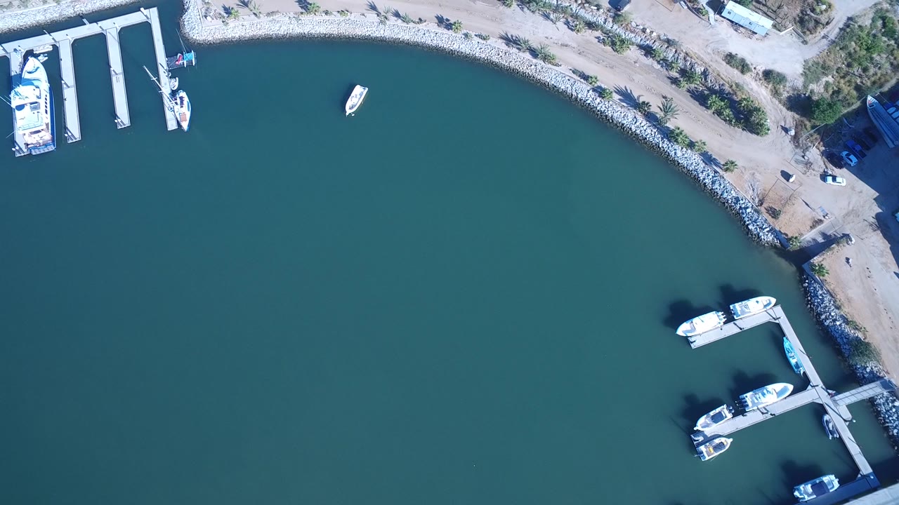 Top-down view of water, shoreline, docks, boats, and a small red-roofed structure.