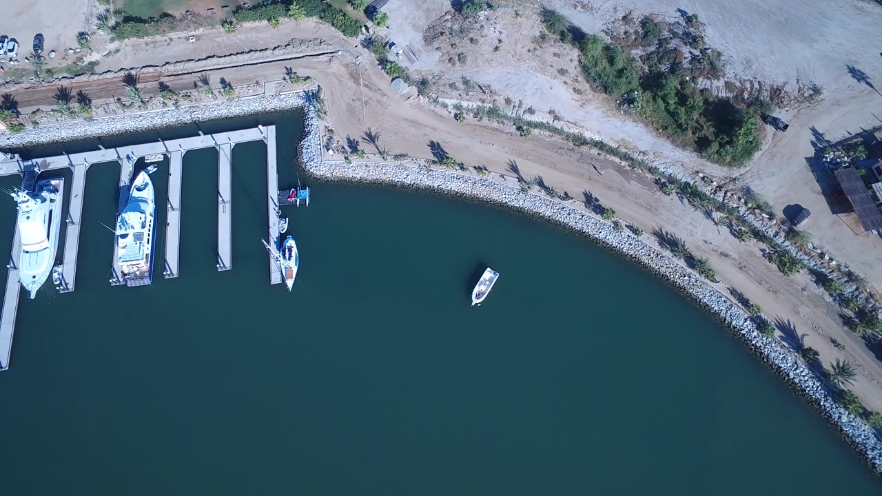 Overhead view in Playita, Baja California Sur, Mexico showing marina slips with boats on the left, green-blue water below, sandy shoreline above, and no visible people.