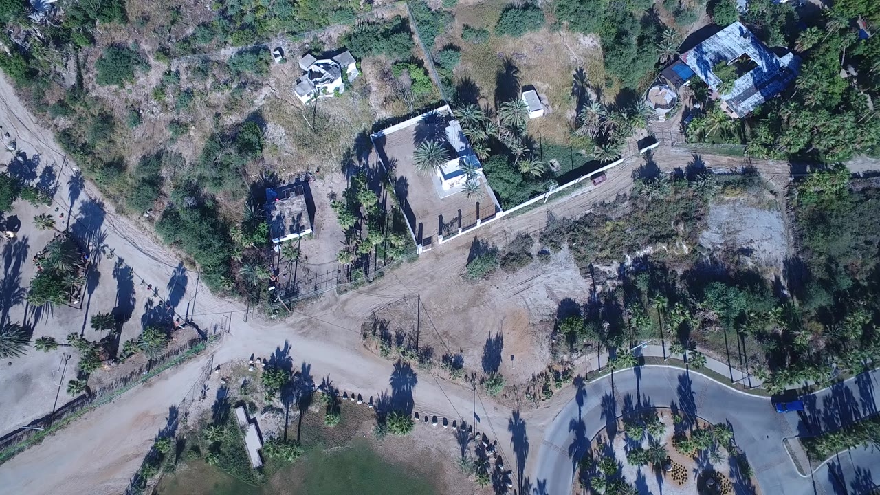 Overhead drone frame in Playita, Baja California Sur, showing dirt roads, concrete paths, private homes, palms, scrubby land, and no visible people.