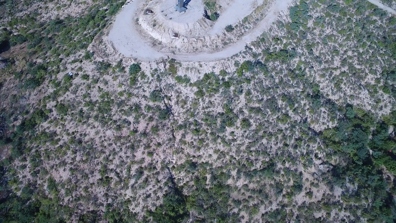 Overhead aerial view of scrubland with the edge of a dirt clearing and cross at the top.