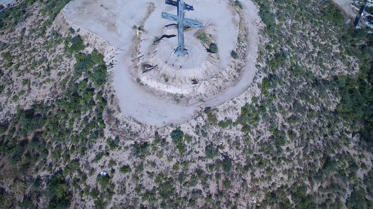 Overhead aerial view of a cross statue on a sandy hilltop