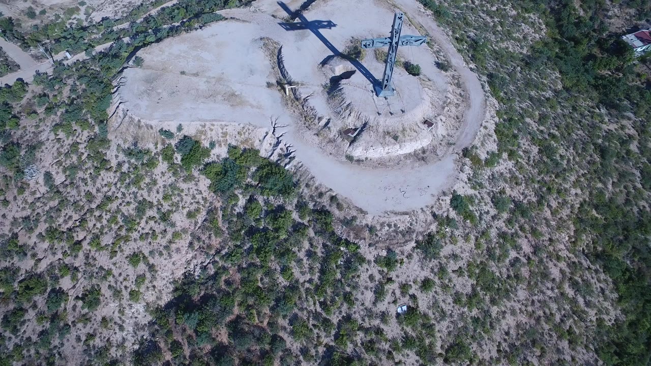 Aerial view of a steel cross on a sandy hill surrounded by scrubland.