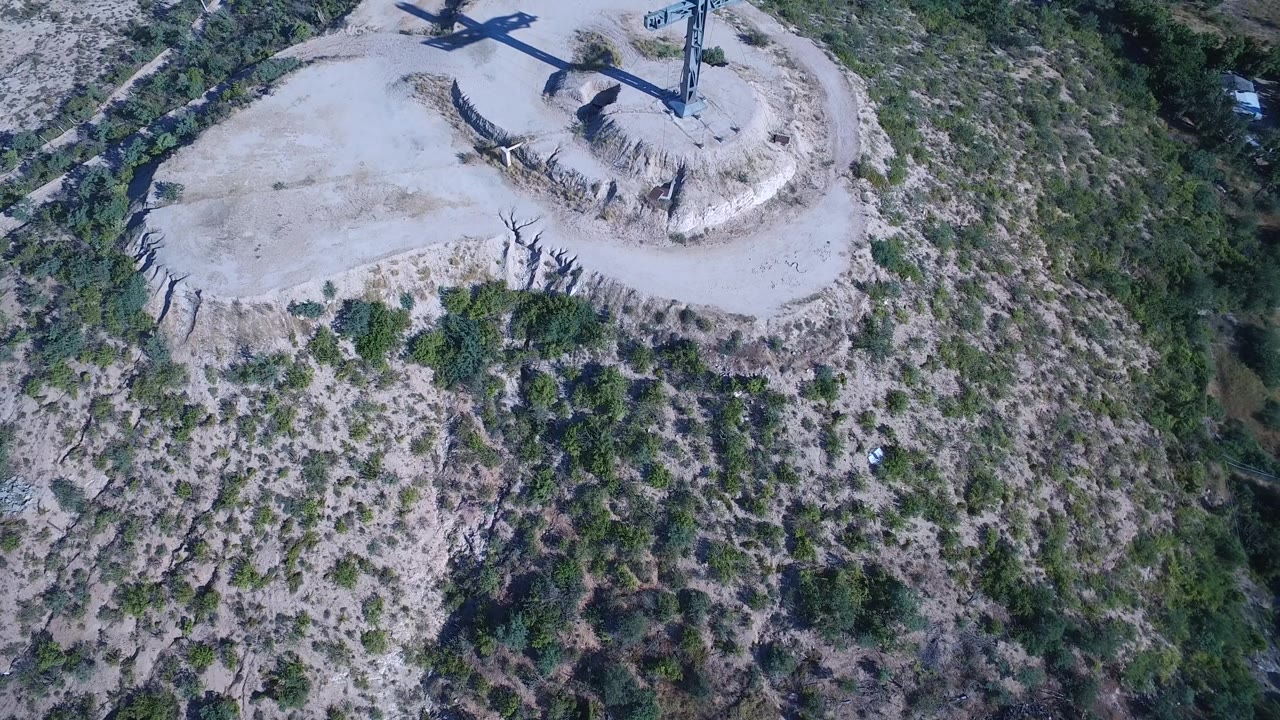 Overhead view of a cross above rocky and grassy mountain terrain.