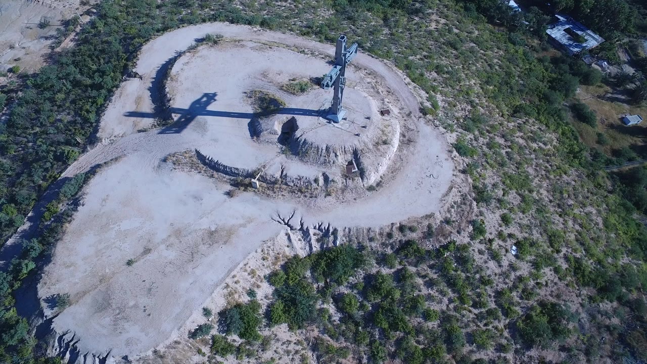 Aerial view of a blue cross on a pale hilltop clearing.