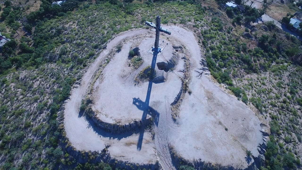 Overhead view of a cross on a sandy hilltop with a long shadow.