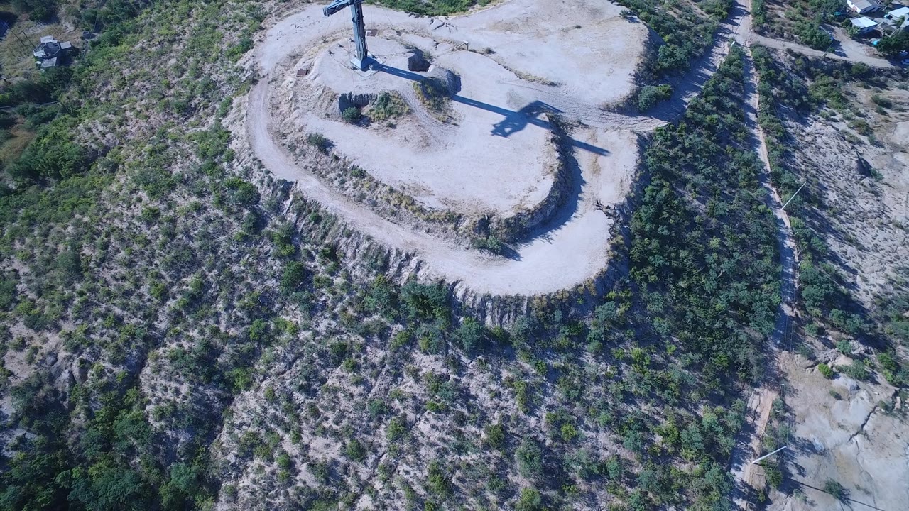Drone-like overhead frame of a crucifix above a green and rocky hillside.