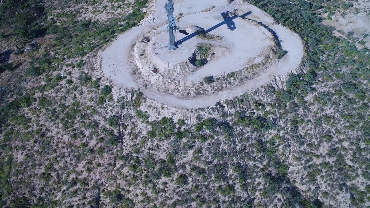 Top-down drone view of a blue cross on a dry hill with brush below.