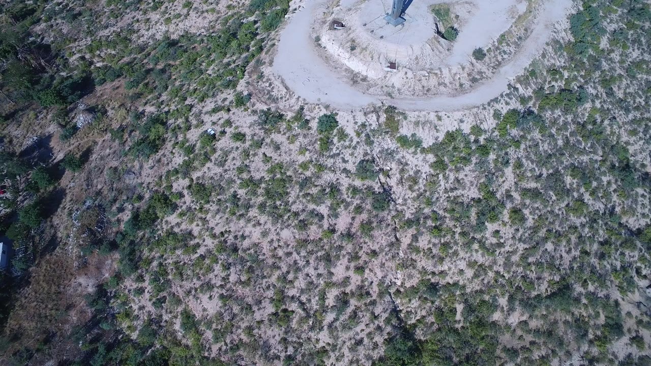 Overhead drone frame in Playita, Baja California Sur showing pale scrub-covered hillside, the edge of a circular dirt landmark area, and no visible people.