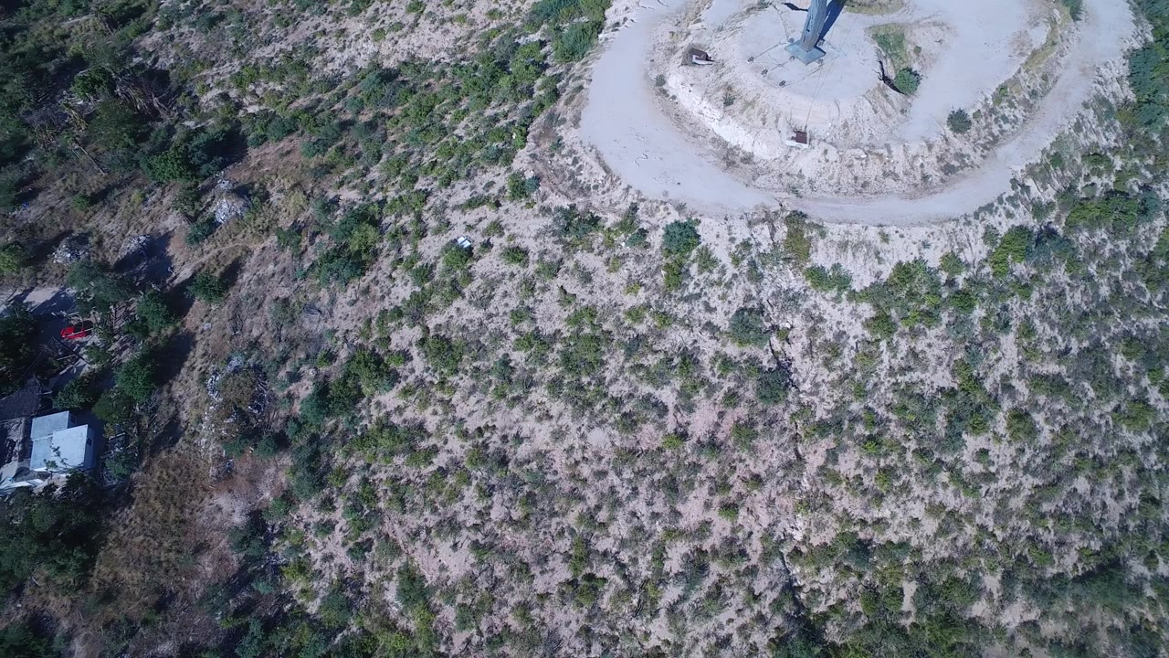 Drone view over hillside scrub with homes and road visible at the side.
