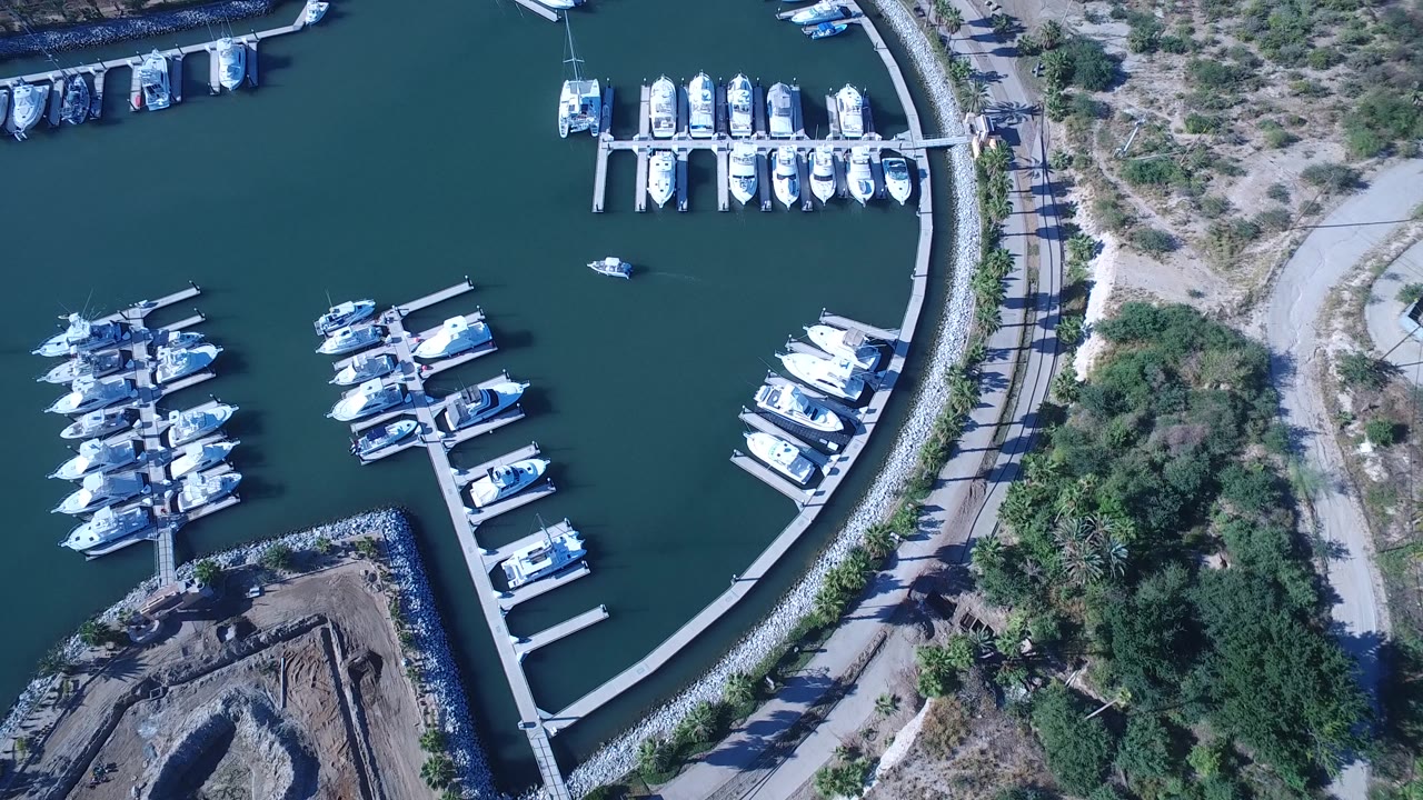 Drone view over clustered boats, docks, water, and shoreline road.