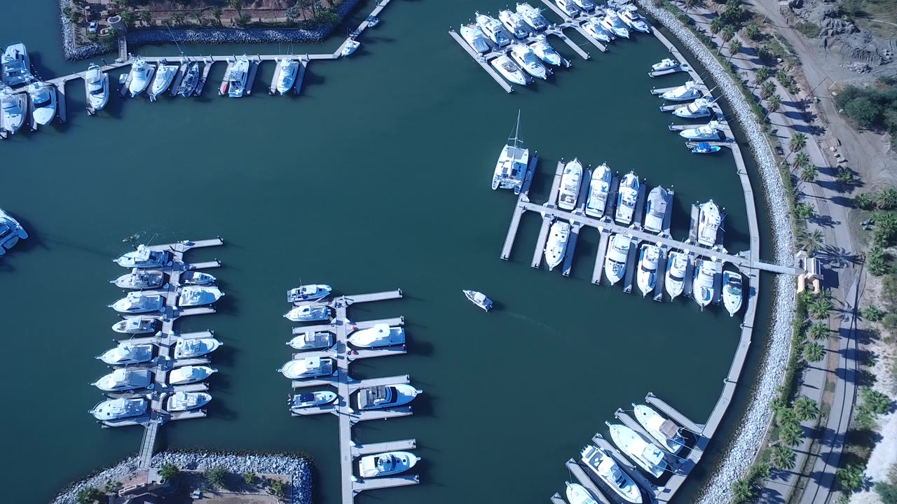 High overhead view of Playita marina water with grouped white boats, floating docks, a curved rock shoreline, and no visible people.