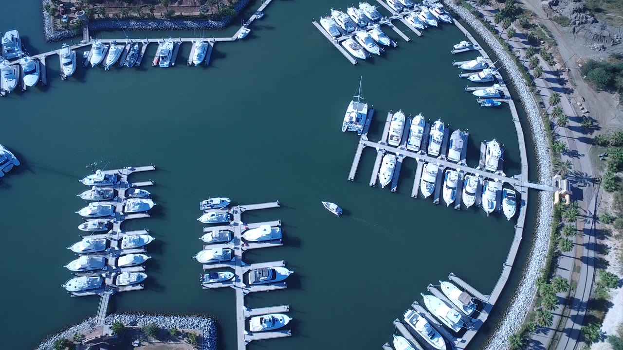 Aerial frame over Playita showing rows of docked boats, open teal water, a curved breakwater road, and no visible people.