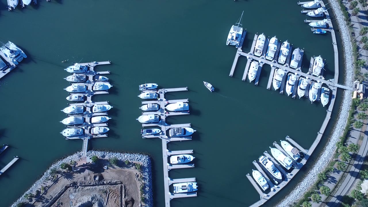 Overhead view of marina docks and moored white boats beside teal water.