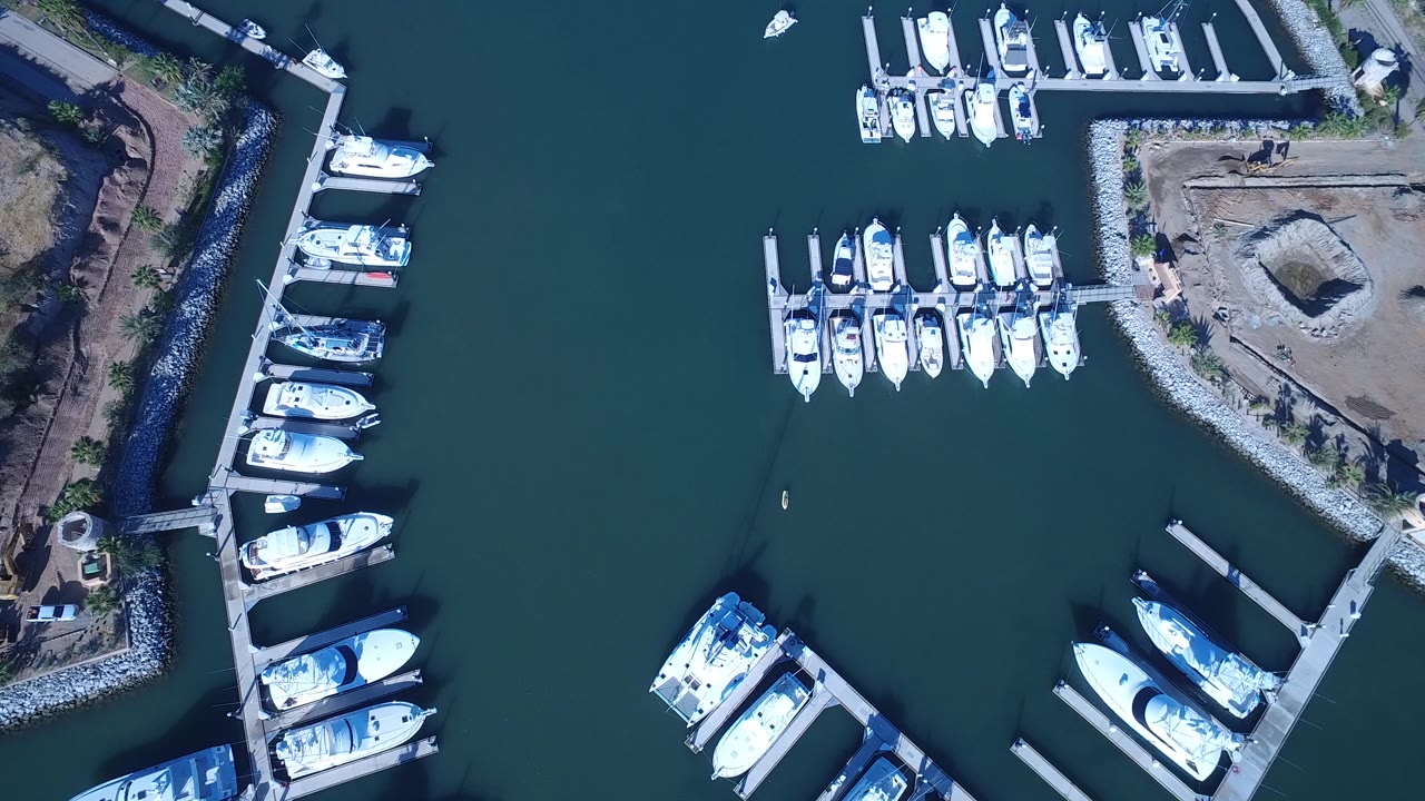 Top-down view of a Playita marina with white boats moored along docks, teal water, rocky shoreline edges, and no visible people.