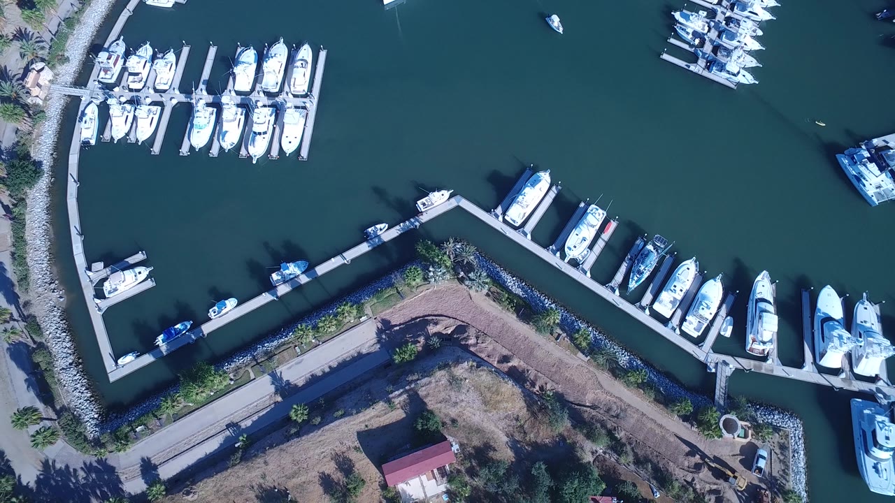 Top-down harbor frame with moored boats on both sides of a dock.