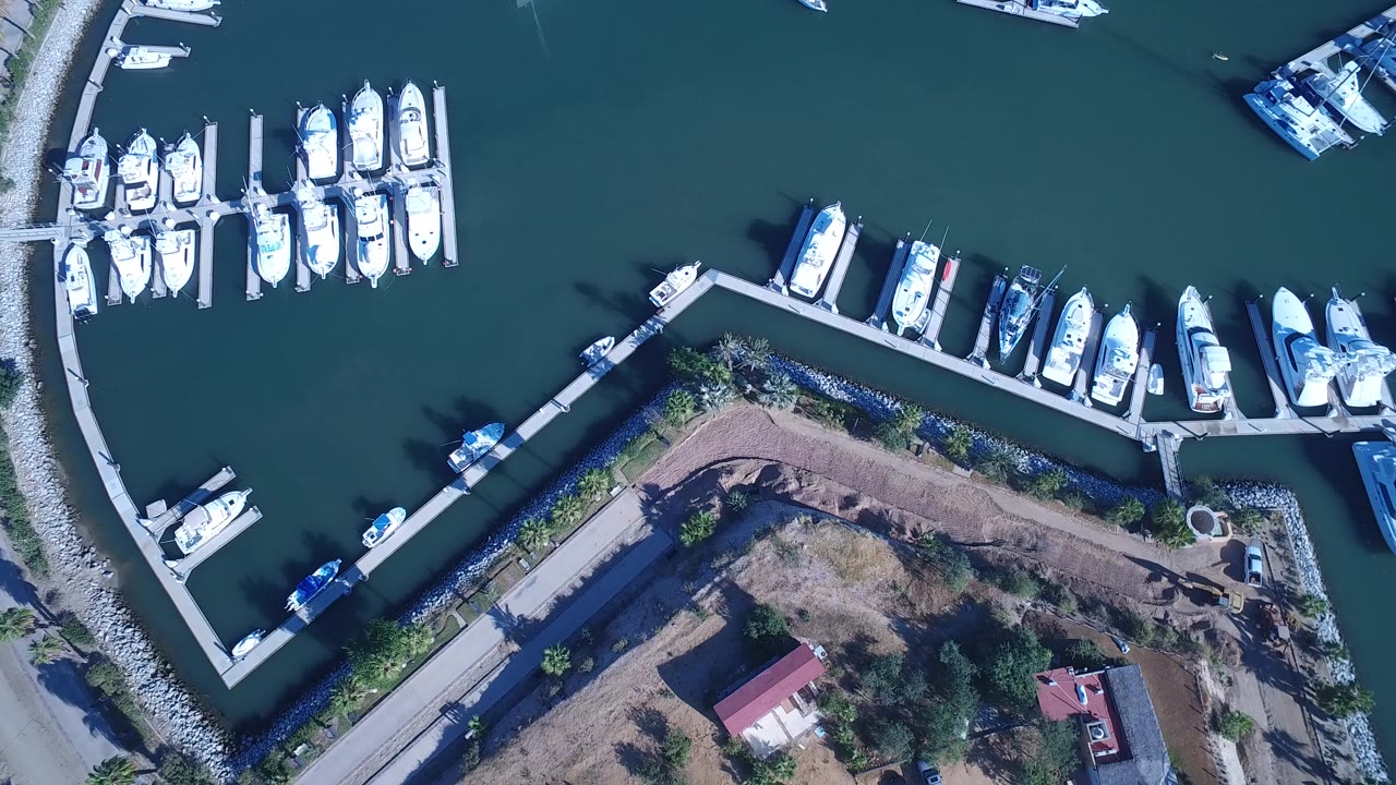 Overhead marina with white boats, teal water, docks, breakwater, and shoreline buildings.