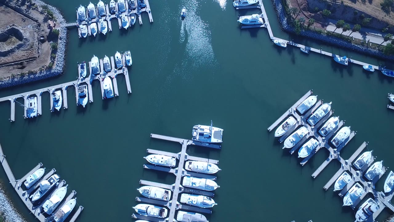 Aerial frame over Playita showing grouped white boats around floating docks, dark teal water between slips, shoreline fill at the top edge, and no visible people.
