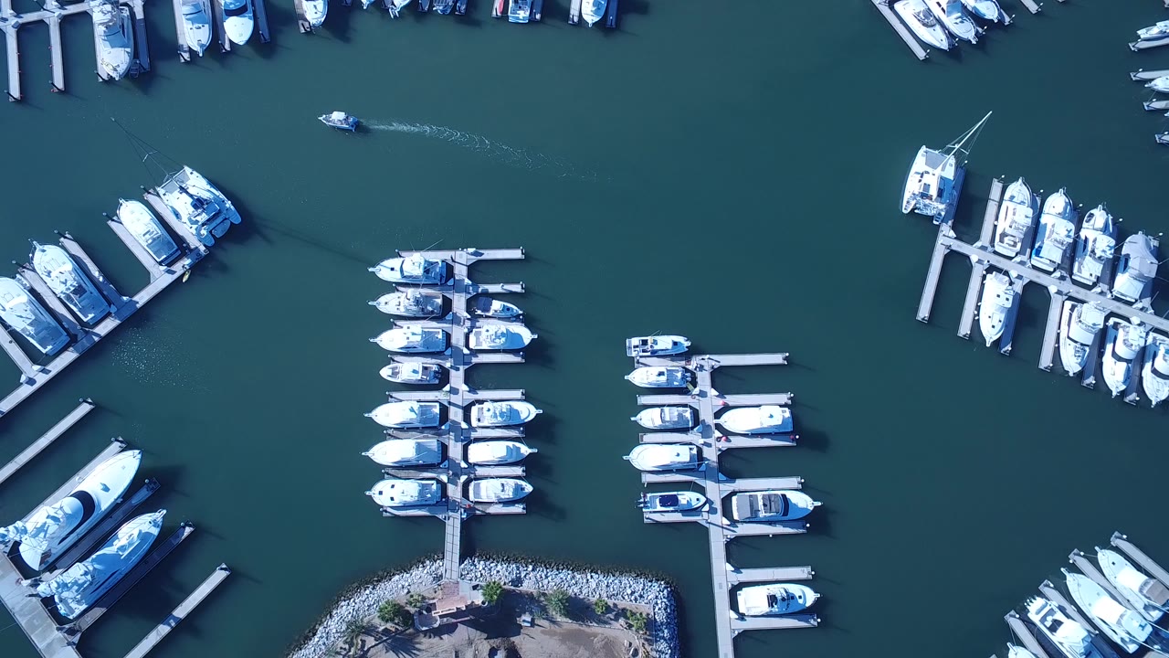 High overhead view of a Playita, Baja California Sur marina with rows of small white and blue boats moored along floating docks and no visible people.