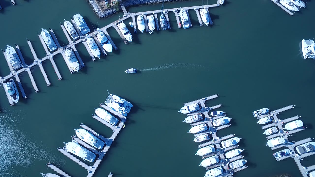 High aerial view of a Playita marina with rows of white boats tied to docks, teal water filling the frame, and no visible people.