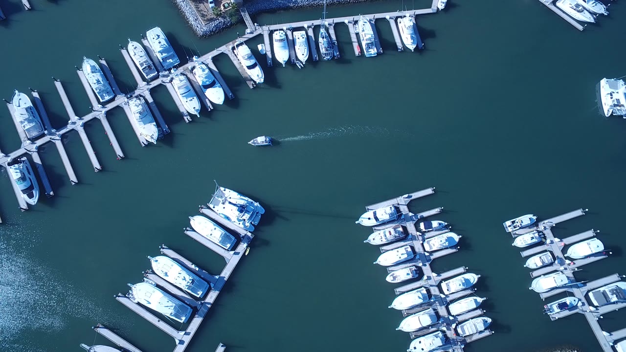 A small boat moves across the open water between docked white boats in Playita, leaving a faint wake and showing no visible people.