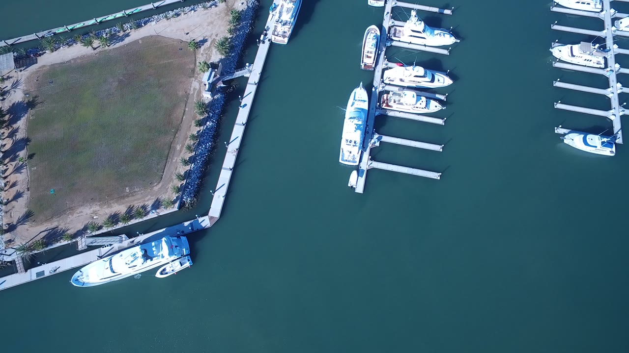 Overhead view of a grass waterfront corner, docks, teal water, and moored white boats.