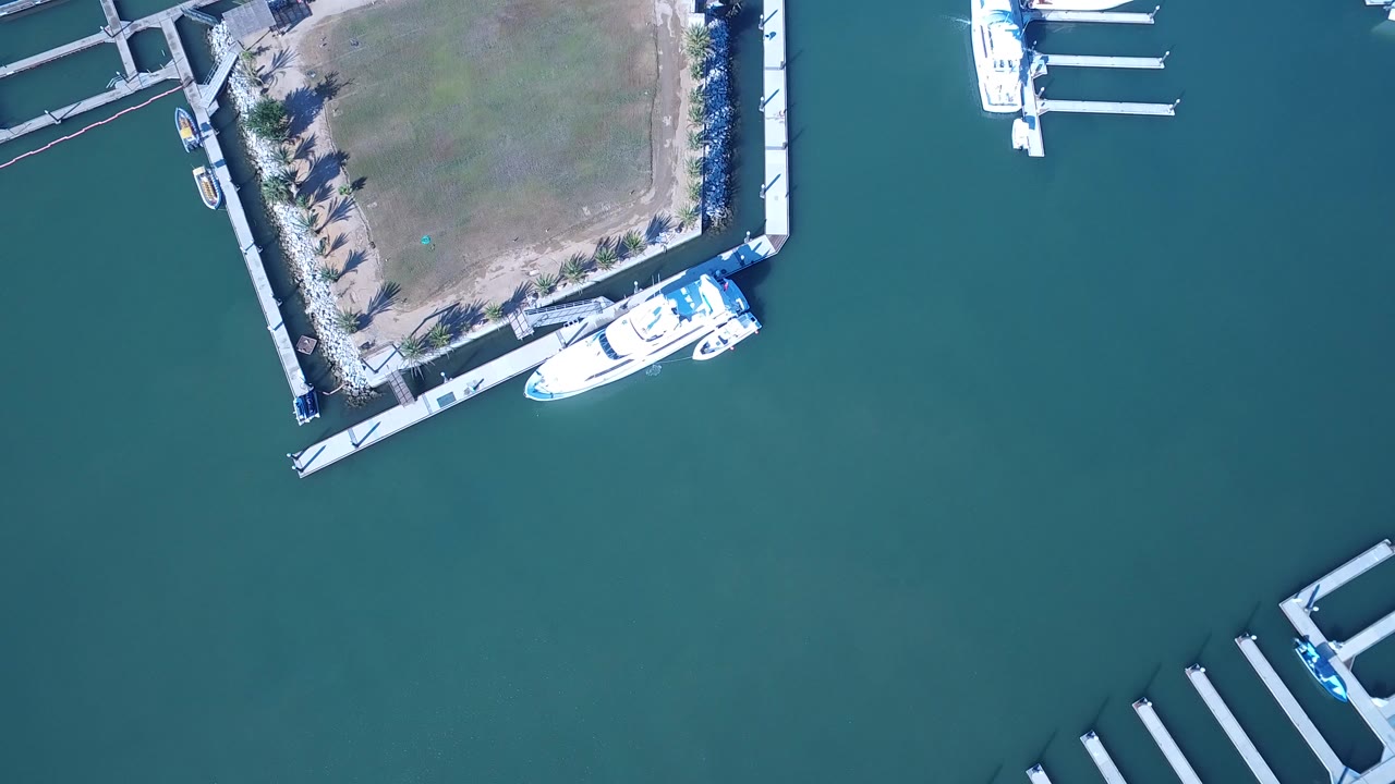 Top-down view over Playita marina water with a square shoreline parcel, white boats at the upper edge, empty finger docks at the lower right, and no visible people.