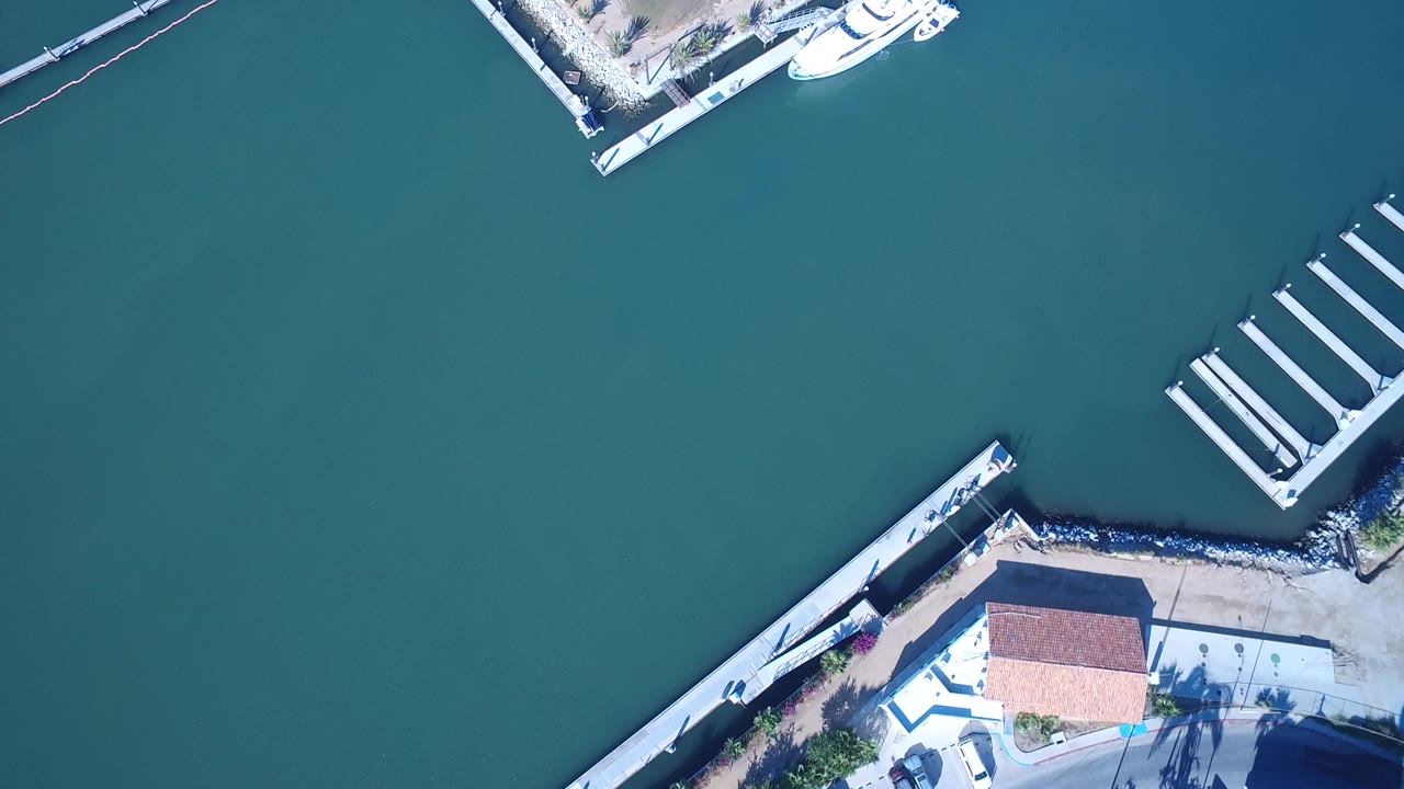 Overhead marina water with dock slips, seawall, and waterfront building corner.