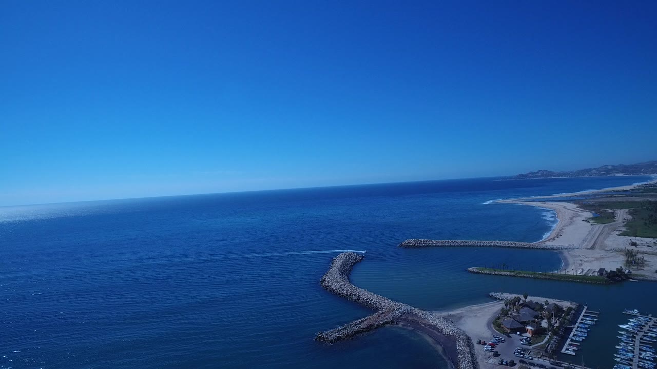 Aerial view of blue ocean, sandy coast, rock breakwaters, and marina docks.