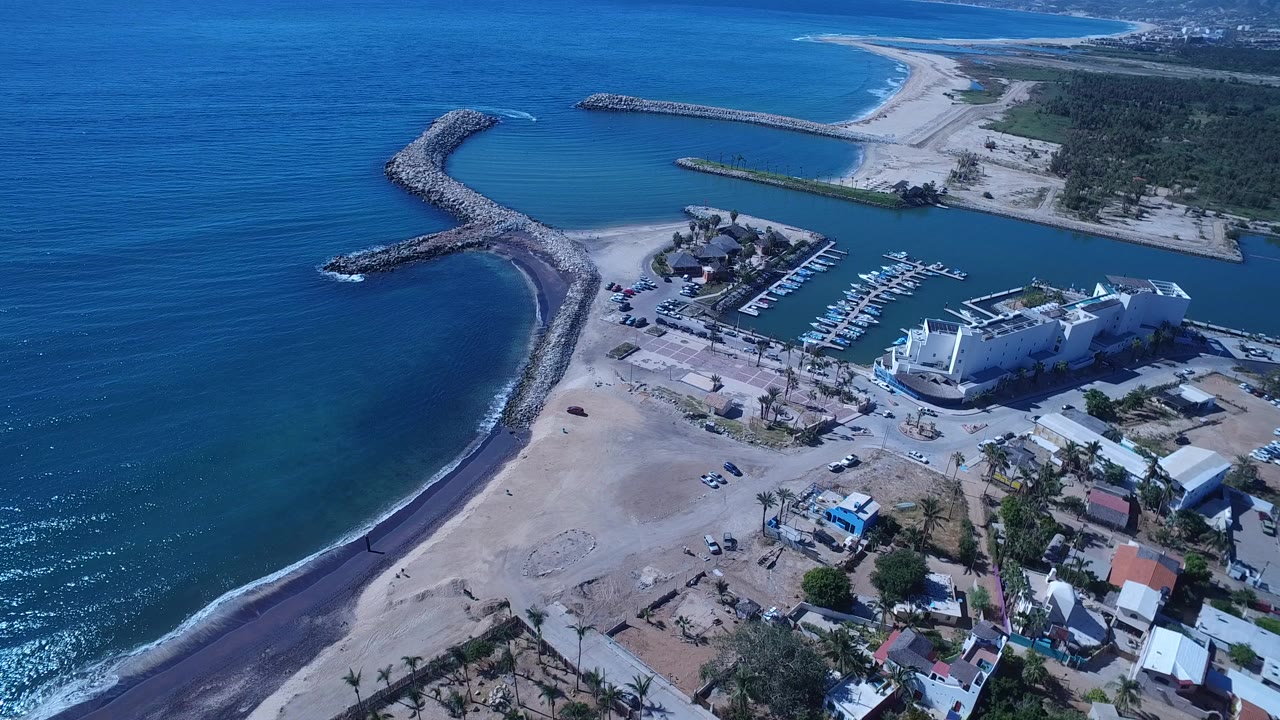 Aerial view of ocean, rock breakwater, beach, marina, and waterfront buildings.