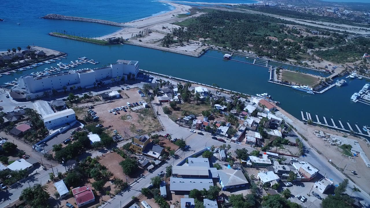 Aerial view of marina water, waterfront buildings, homes, beach, and breakwater.