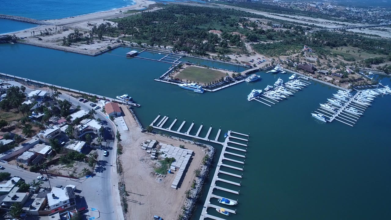 Aerial view of a marina with docks, boats, shoreline, and ocean beyond.