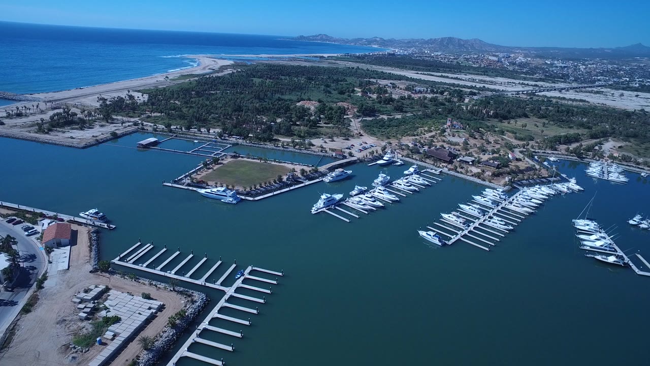Aerial view of marina docks, docked boats, blue bay water, beach, and ocean beyond.