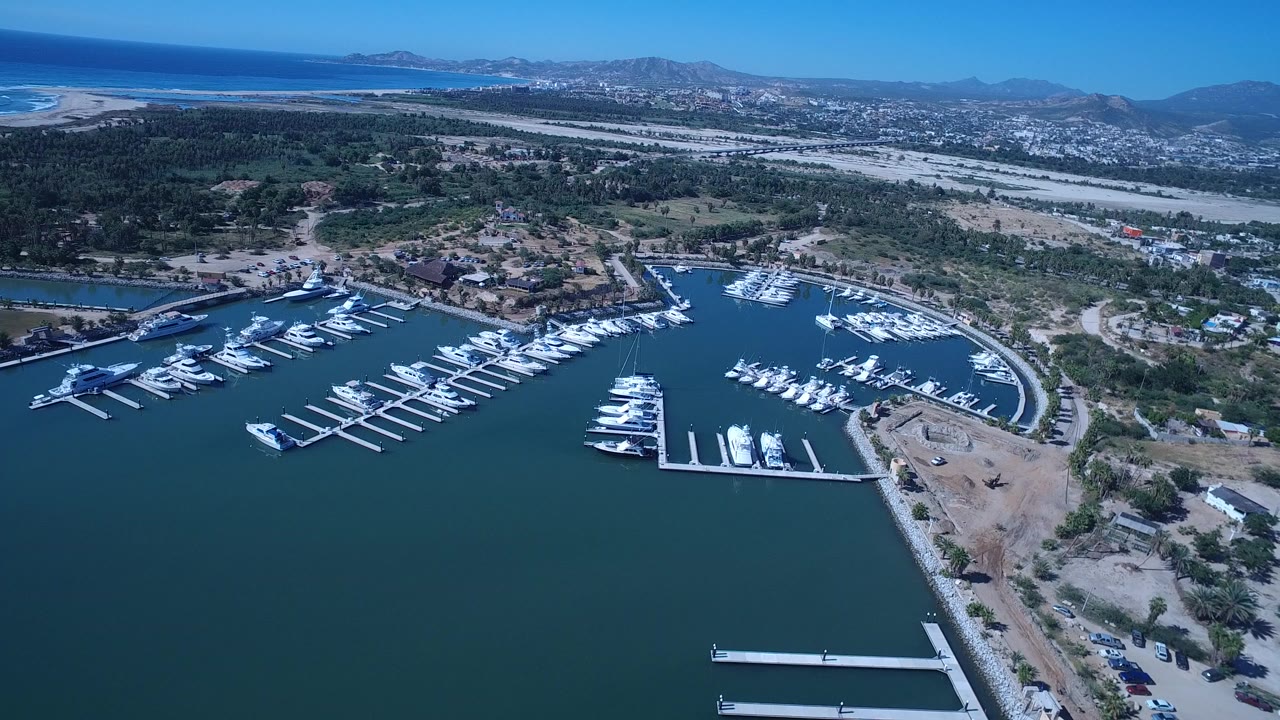 Aerial view of a marina with small boats, docks, shoreline, and distant mountains.