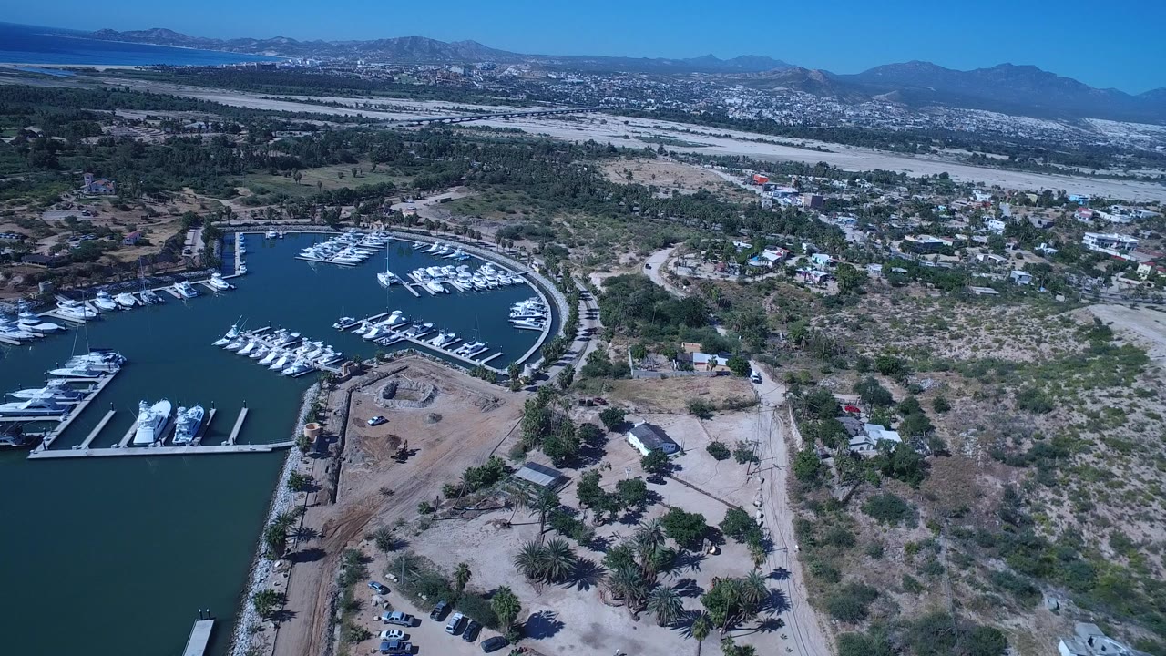 High aerial view of marina water, boats, dry land, roads, and distant mountains.