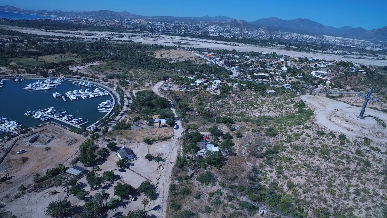 Aerial view of marina water, boats, dry scrubland, houses, and distant mountains.