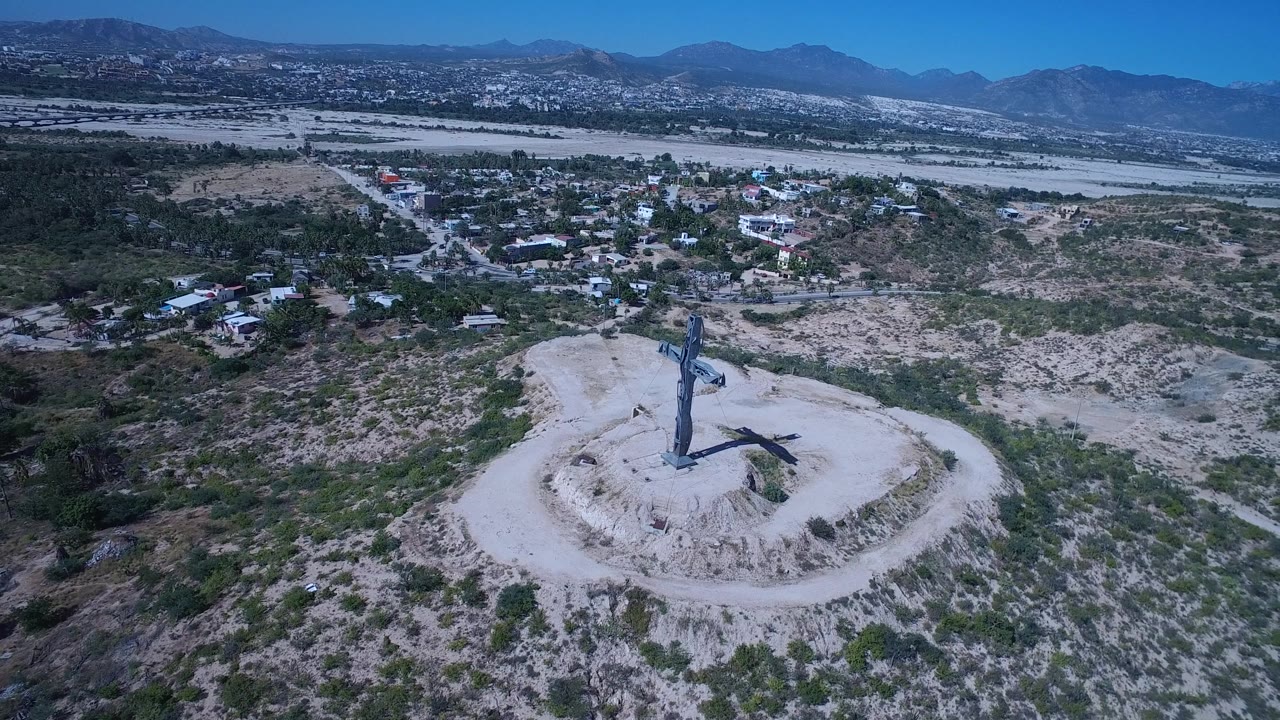 Hilltop cross seen from above with arid terrain and distant ridges.