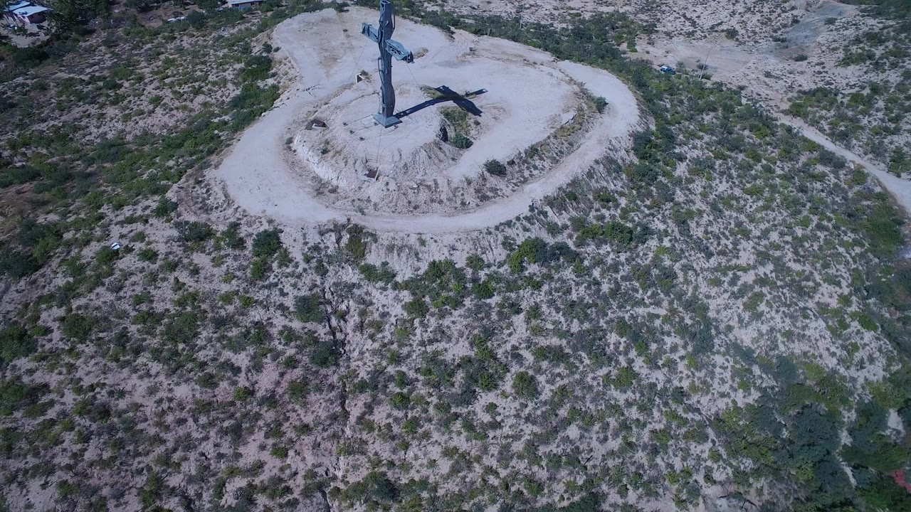 Aerial view in San Jose del Cabo, Mexico of a large blue cross on a pale circular mound surrounded by scrubby hillside, with no visible people.