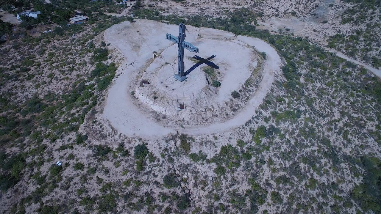Aerial view of a cross on a pale hilltop surrounded by brush.