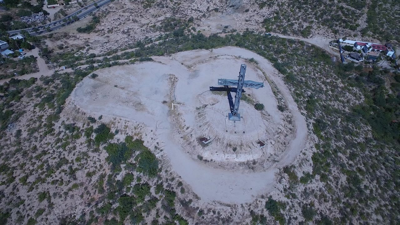 Elevated view of a blue cross on a pale hill with buildings nearby.