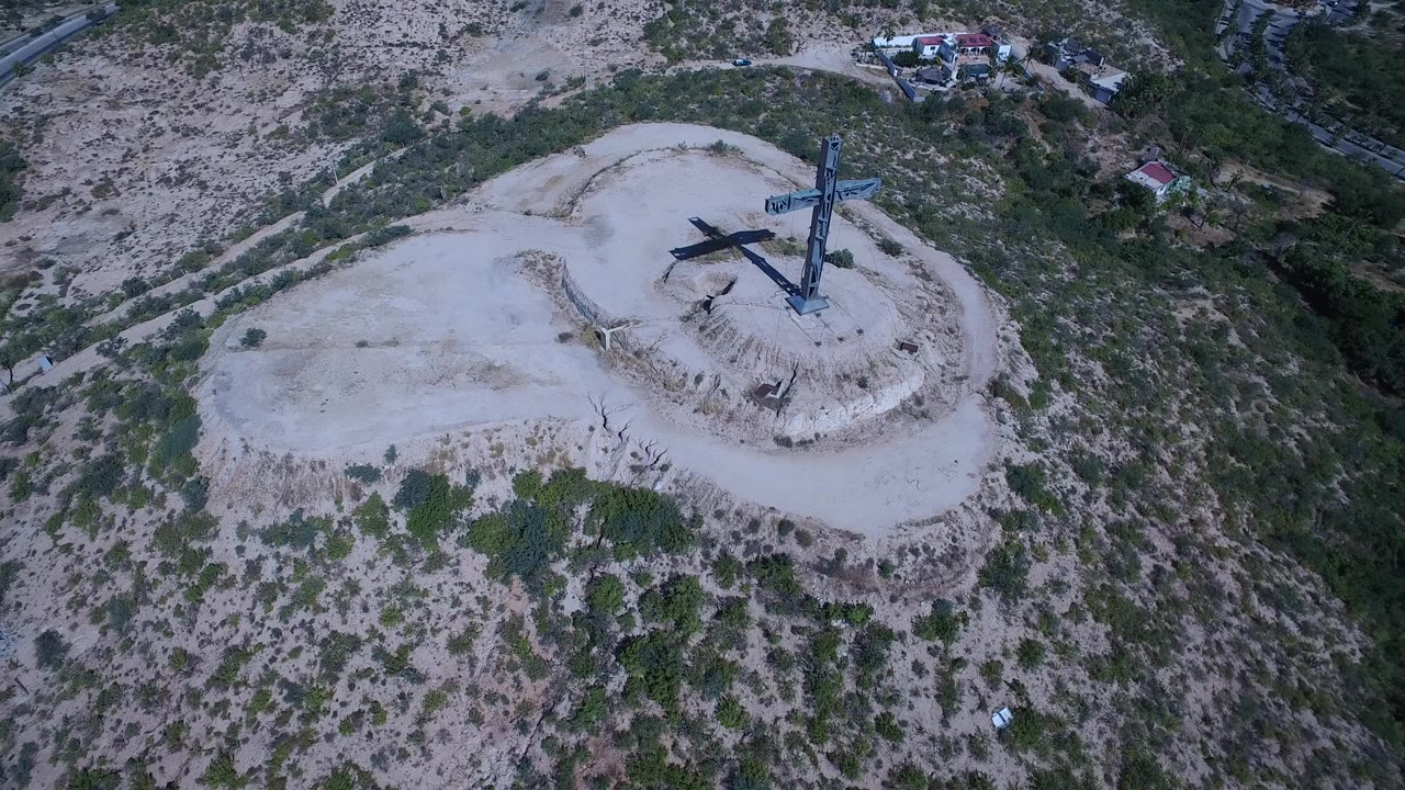 Aerial view of a large cross structure on a pale hilltop clearing.